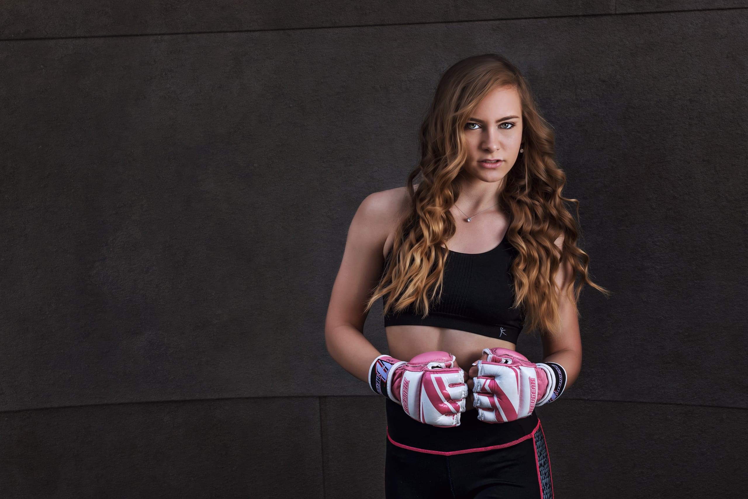 A young woman holding pink boxing gloves against a textured studio backdrop