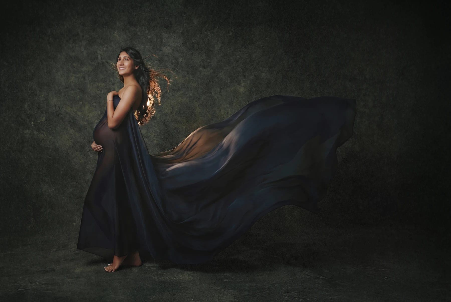 A maternity portrait with flowing navy fabric against a green backdrop