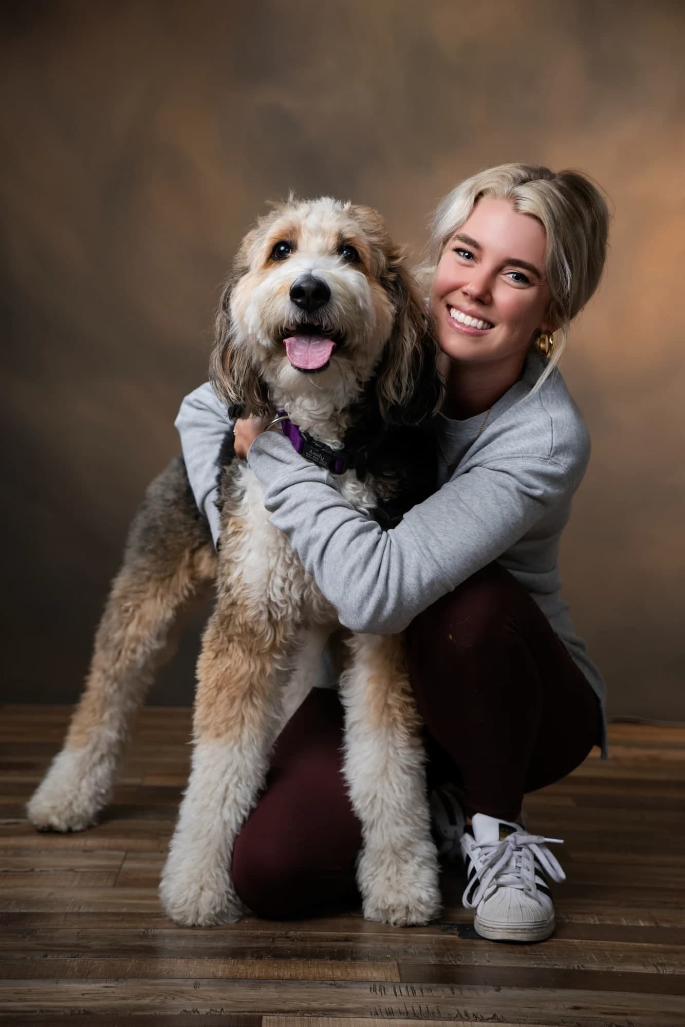 A smiling woman embracing her shaggy dog in a studio portrait