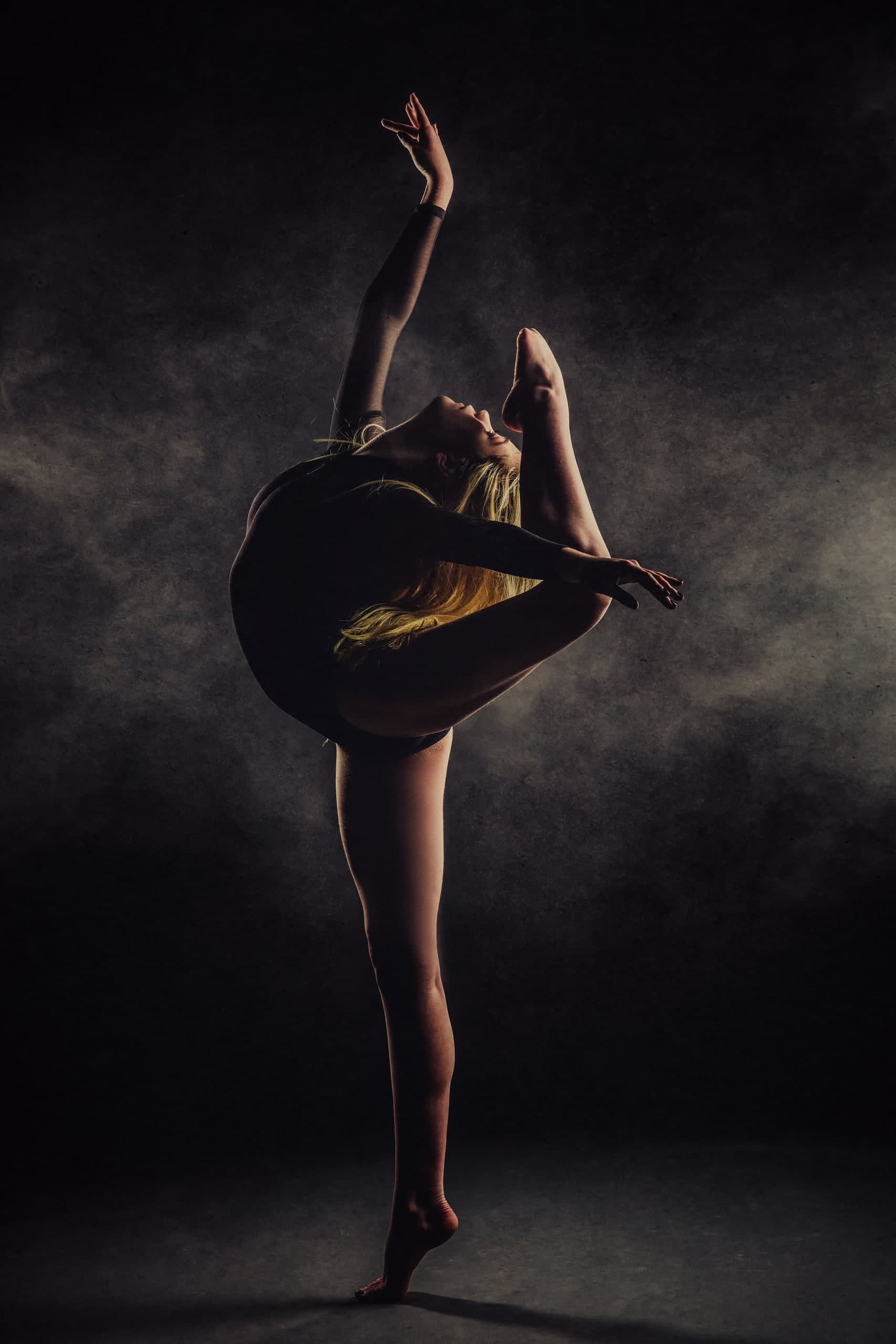 A dancer extending one leg upward against a dark studio backdrop