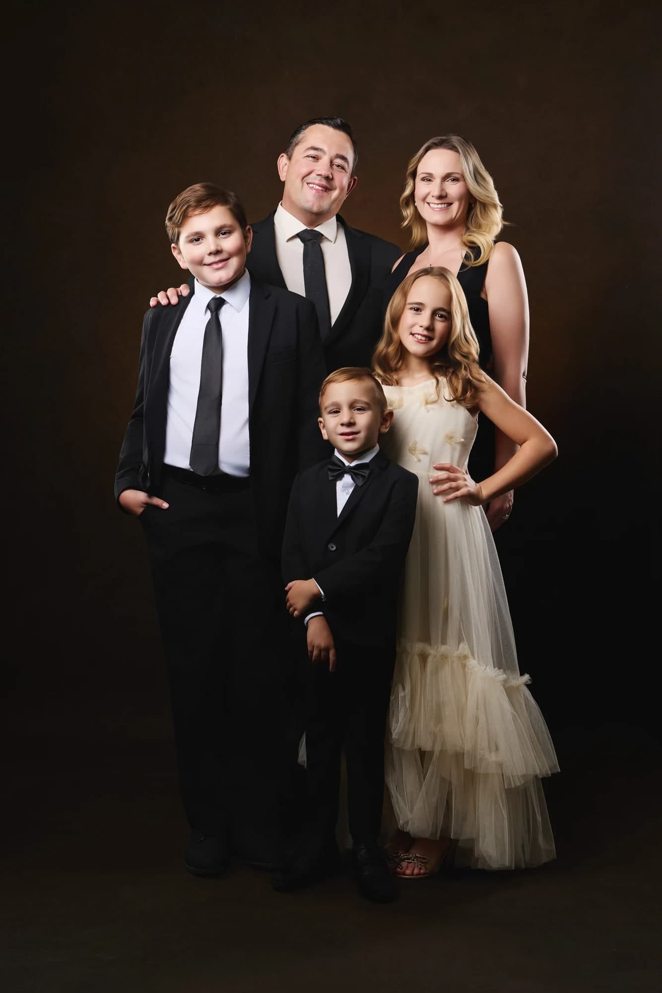A family in formal clothing seated together against a warm studio backdrop