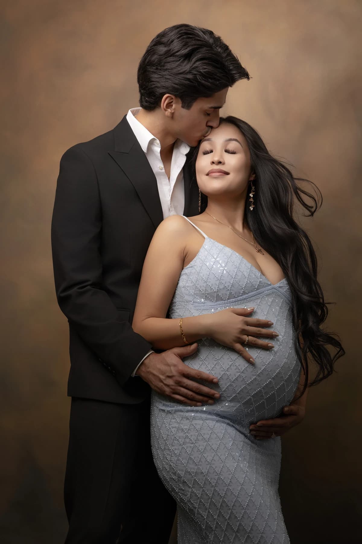 Expectant parents embracing in a blue gown and dark suit