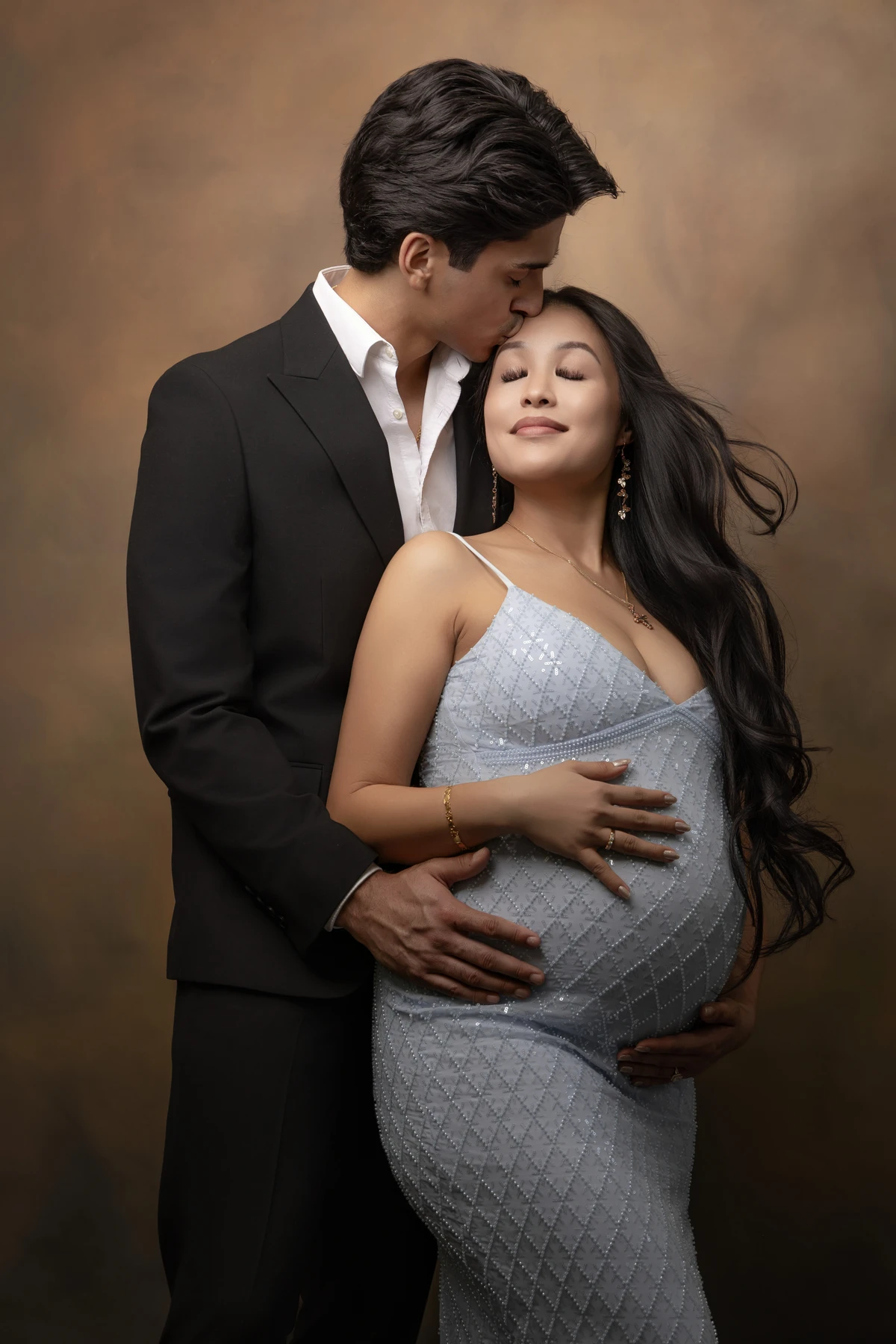 Expectant parents embracing in a blue gown and dark suit