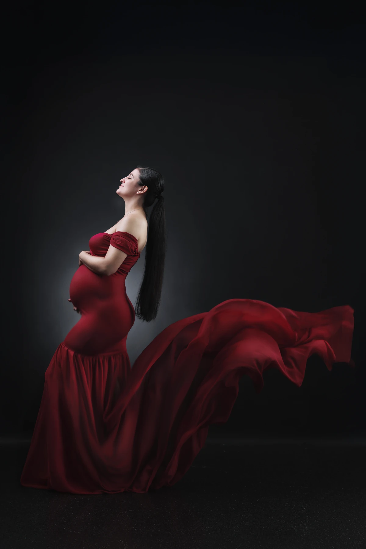 Maternity portrait with sculptural red fabric against charcoal