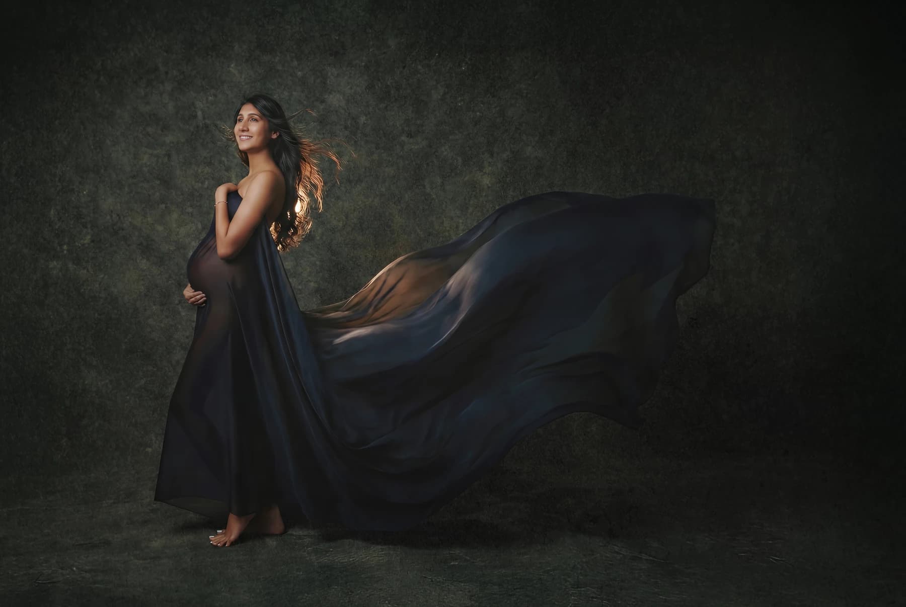 Maternity portrait with a flowing navy gown against a green backdrop