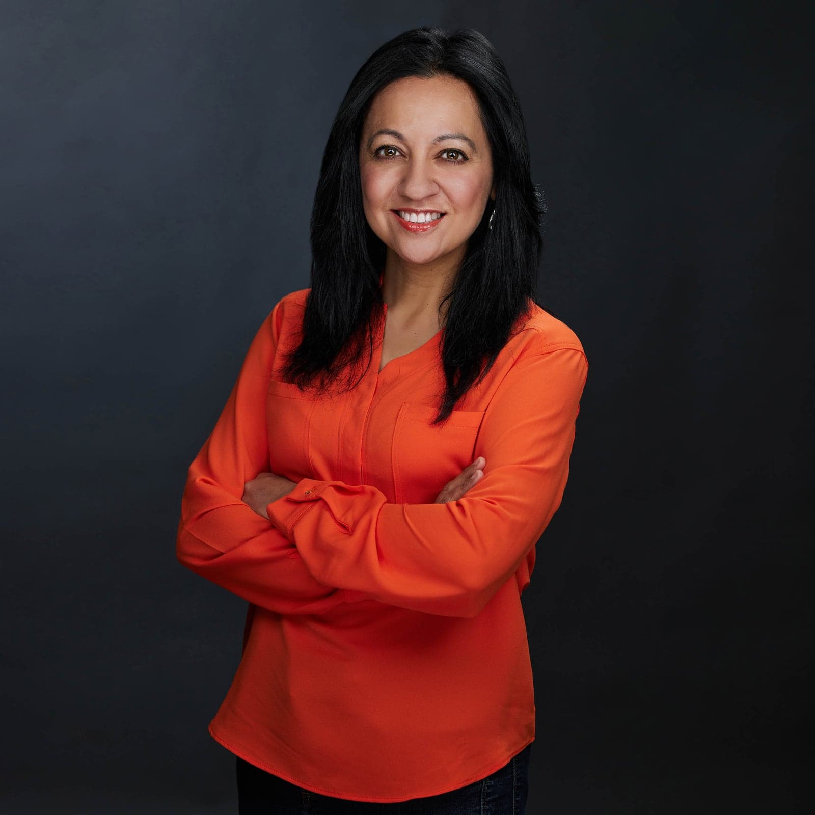 A woman in an orange blouse against a dark studio background