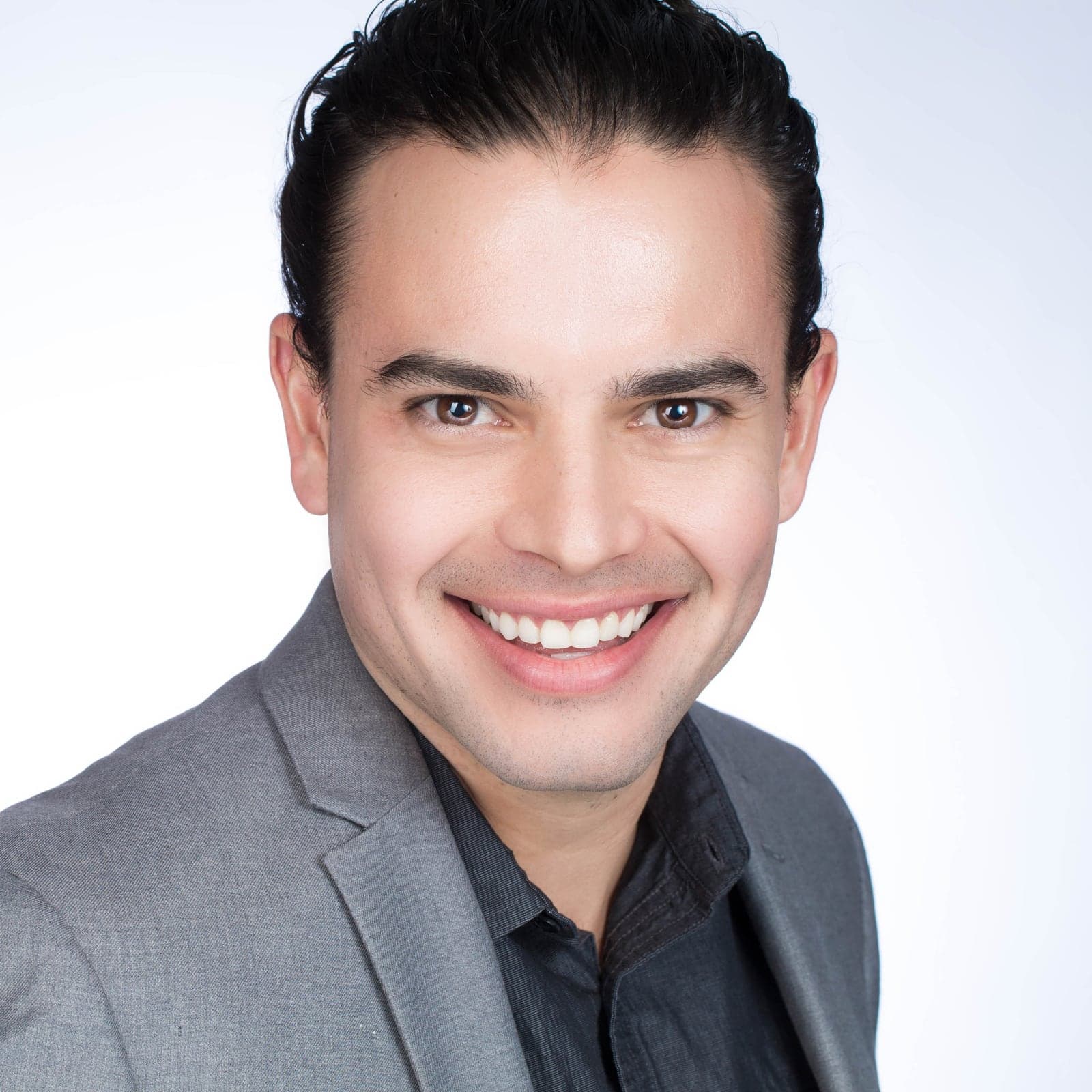 A smiling man in a grey jacket against a white studio background